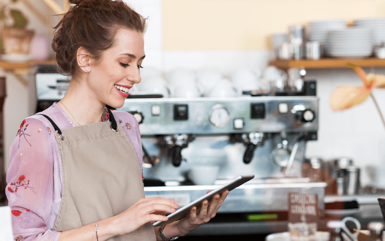 A woman working in a coffee shop works on a tablet