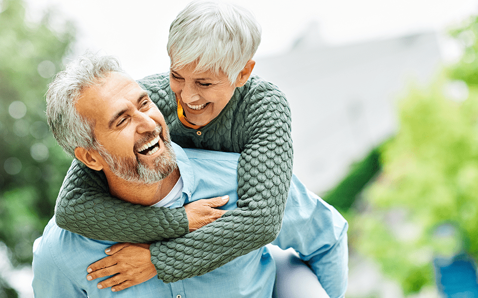 A woman is getting a piggy back ride from her husband. They are both smiling.