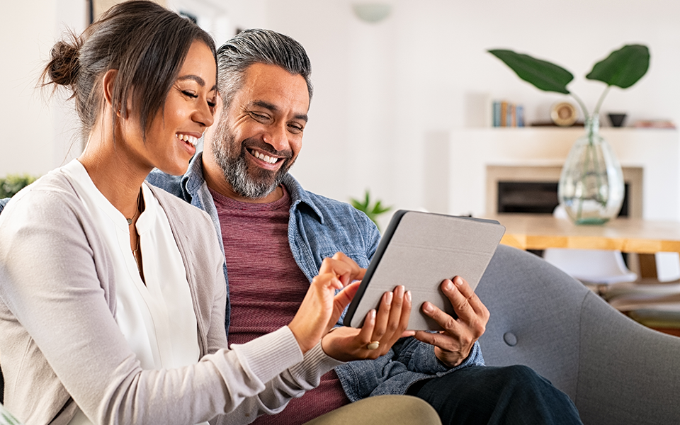 A man and woman are seated on a sofa, working together on a tablet