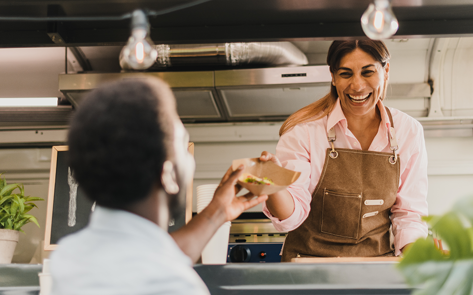 A woman in a food truck hands a customer a basket of food