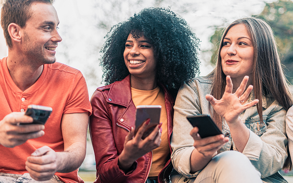 A group of three people are seated next to each other. They are all holding smart phones in their hand