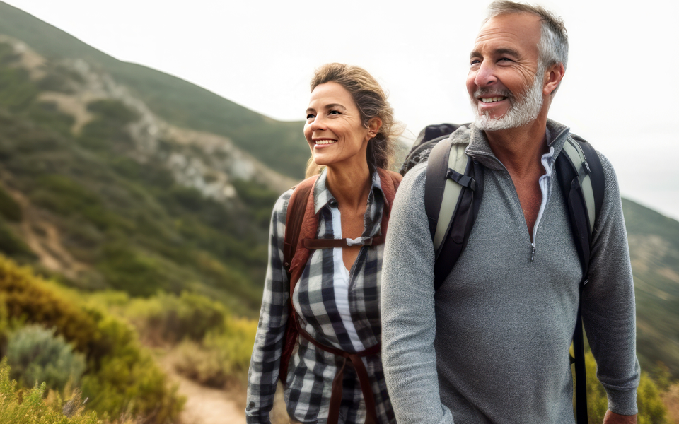 A man and woman are outside on a hike. They are wearing backpacks and they look happy.