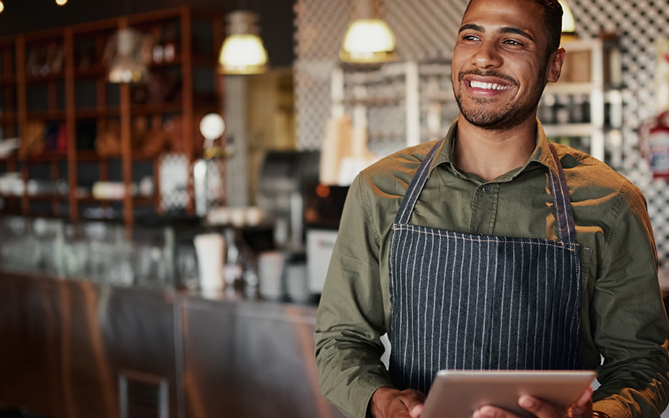 A man is standing in a cafe, wearing an apron