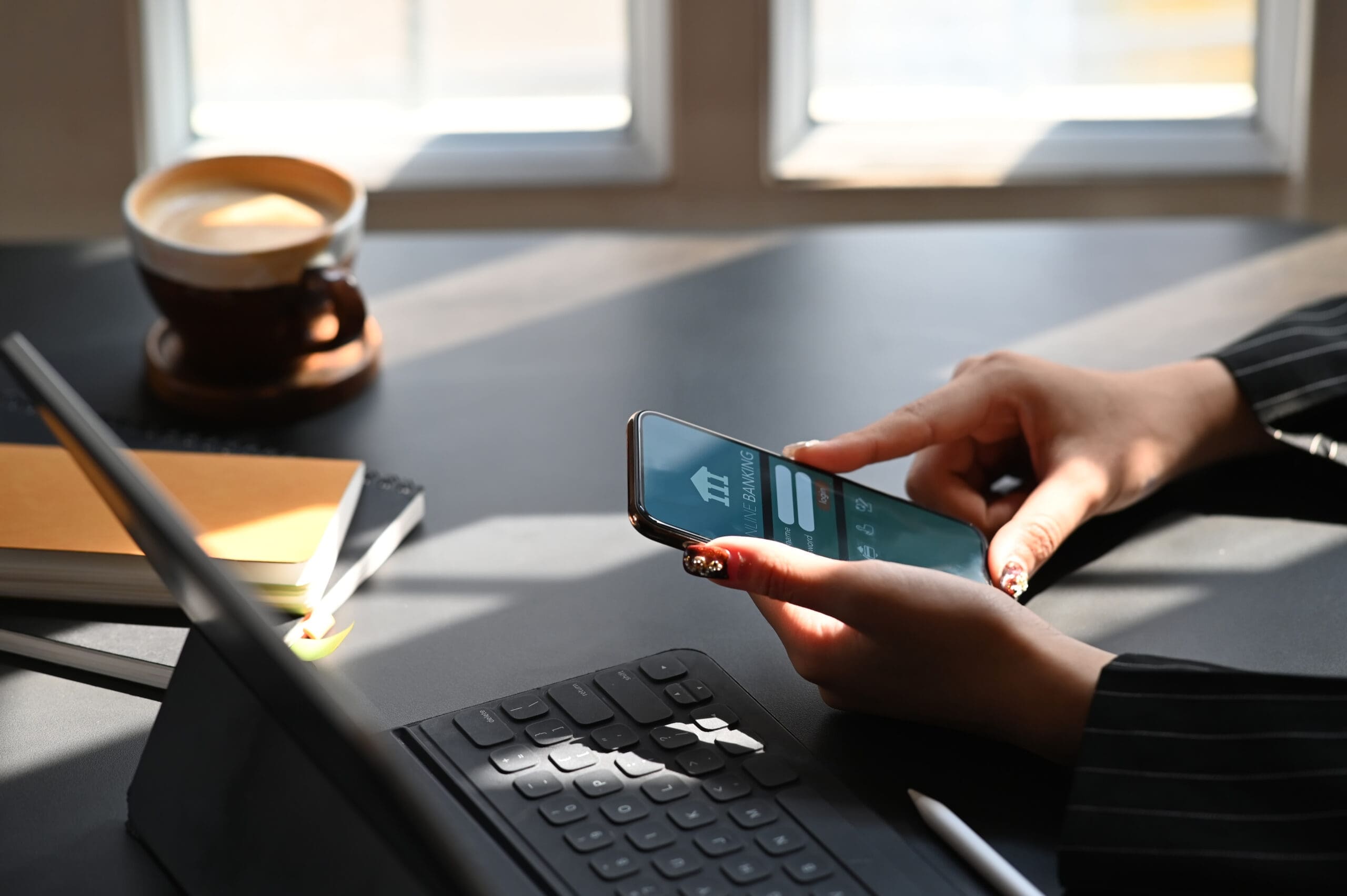 Cropped shot of executive woman holding smartphone in hands while doing online financial transaction by her smartphone in front computer tablet at the modern working desk