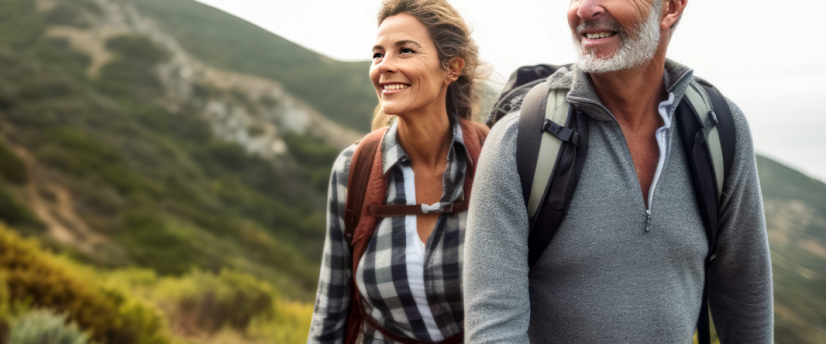 A man and woman are outside on a hike. They are wearing backpacks and they look happy.