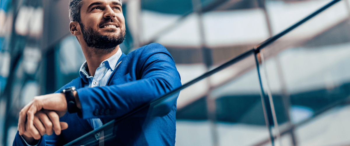 A man in a suit stands at a balcony. He is looking off into the distance
