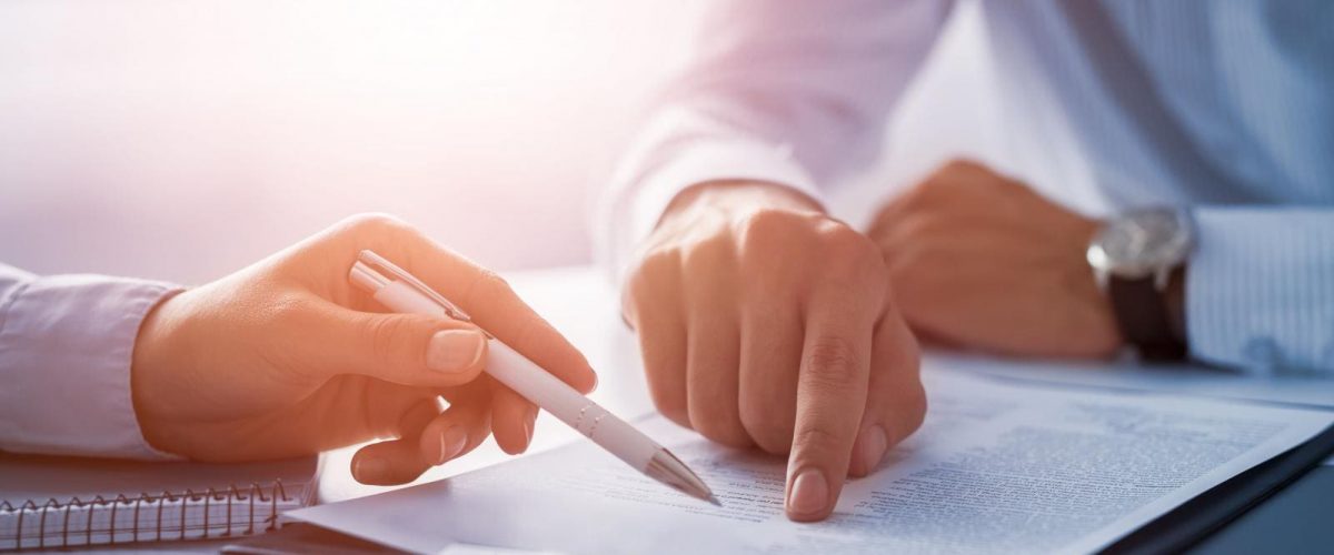 Close of up hands, one hand is holding a pen pointing to a particular place in the paperwork